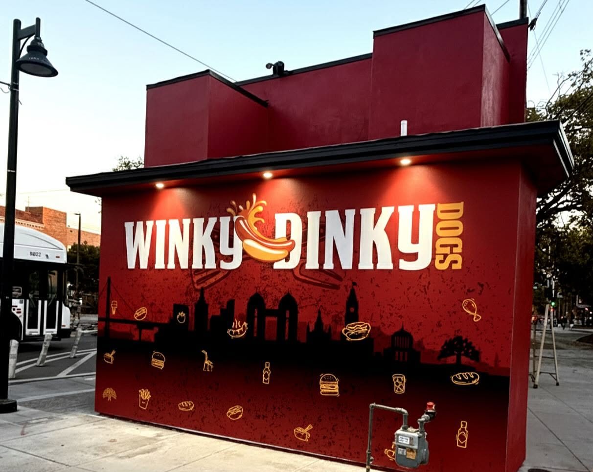 Winky Dinky Dogs building in Oakland, wrapped in red with the logo over an Oakland skyline and food illustrations